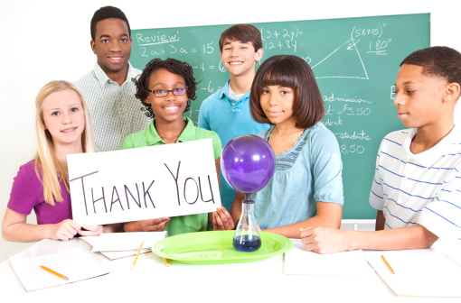 Junior high students and teacher in science class.  Students hold a thank You sign.  Science experiment on lab table.  Thank a Teacher.   