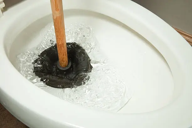 A rubber plunger is working on a toilet clog and displacing water.