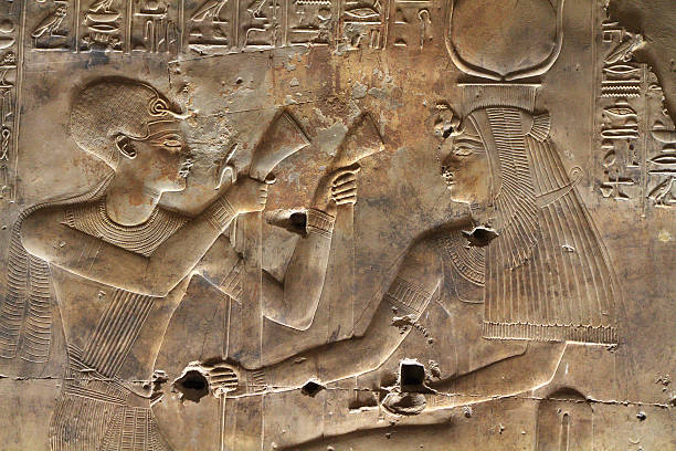 Wall Relief, Sanctuary of Isis, Seti I&#8217;s Temple, Abydos, Egypt "Raised relief, or bas relief, in the Sanctuary of Isis, part of the Temple of Seti I, Abydos, Egypt.  The relief depicts the 13th century BC pharaoh Seti I (also Sethos I, Sethi I, Sety I and Menmaatre), on the left, holding two lotus plants (the blue water lily), symbol of the continuous cycle of death and rebirth.  The figure on the right is Isis who wears the solar disk and horns rather than the throne-shaped headgear with which she is normally associated.  Begun by Seti I but completed by his son, Ramesses II the temple of Seti I at Abydos is one of the finest buildings in Egypt." abydos stock pictures, royalty-free photos & images