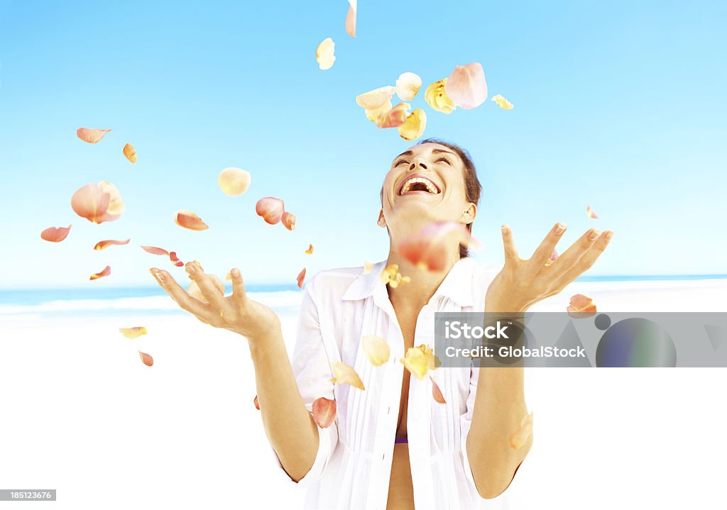 Lose yourself in the moment Happy woman standing on a beach throwing rose petals up into the air Adult Stock Photo