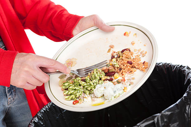 Emptying food leftovers into rubbish bin Close-up of a woman sweeping the leftovers from a meal into a domestic garbage bin. The background is pure white. leftovers photos stock pictures, royalty-free photos & images