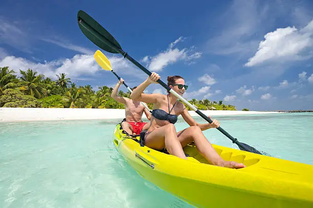 couple paddling in kayak near island full of palmtrees