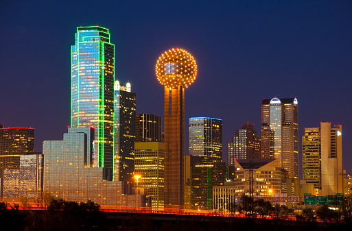 Dallas skyline at dusk / twilight / early evening with the Bank of America Plaza and Reunion Tower prominently shown and prominently lit.  Also featuring light trails from Interstate 30 freeway.