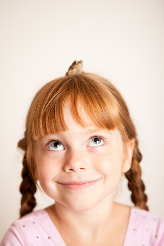 Close up head shot portrait of little brown-haired child girl. Cheerful kid against white studio wall background