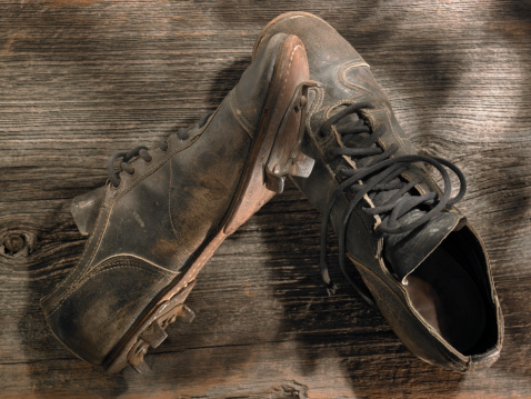 A pair of old weathered baseball cleats, warmly lit on an old wood background. Tinted slightly to add to the nostalgic feel.