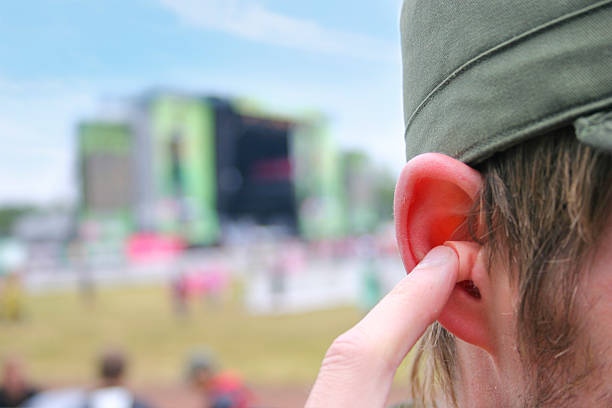 Earplugs at a music festival A young guy using earplugs at a music festival to protect his ears from the noise. Stage of music festival in the back. stopper stock pictures, royalty-free photos & images