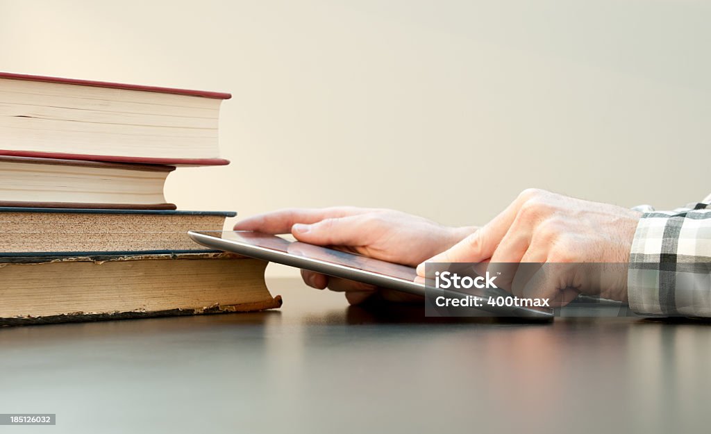 Studying using a Digital Tablet Male hands using a digital tablet next to a pile of old books. Abstract Stock Photo