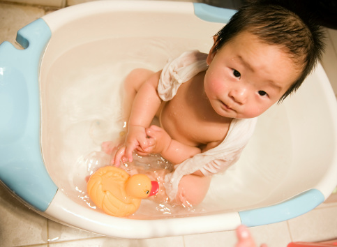 cute little girl lying on bath in bathroom with water, looking at camera