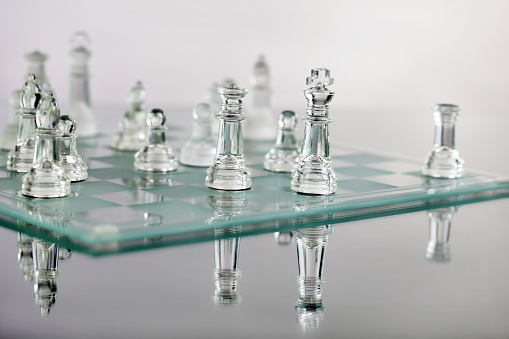 Lone Chess Queen piece on a square on an empty chess board highlighting a feeling of isolation. The Queen is too big for the chess board - egotistical!