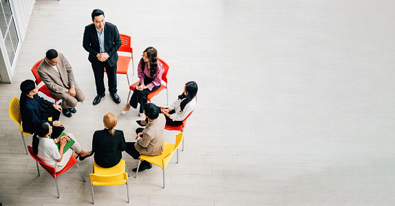 From above, diverse group collaborates in bustling office, engaged in teamwork and discussions. A businessman and businesswoman sit at a conference, providing space for your business meeting concept.