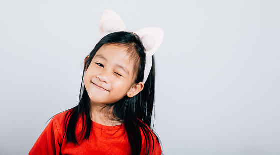 A joyful Asian kid girl in a red t-shirt beams with happiness her open mouth revealing a big smile and confidence. Isolated portrait of a cheerful child on a white background.