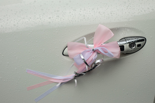 Pink bow on car door. Pink ribbon on transport. Arrangement of transport for wedding. Bow made of fabric.