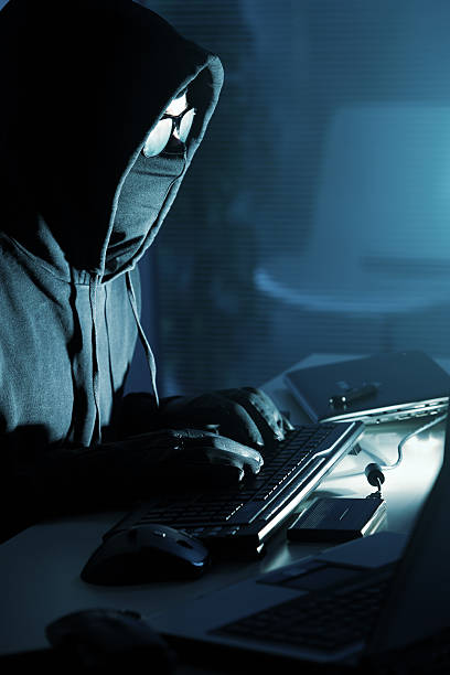 A hoodie clad hacker is stealing data on a computer Young male thief stealing data from computer clad stock pictures, royalty-free photos & images