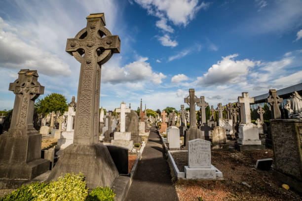 In an Irish cemetery, an ancient stone cross stands, weathered by time yet steadfast in its presence. Carved with intricate detail, it bears the weight of history and reverence. At its center, a solemn depiction of the sacred heart radiating with eternal love and compassion, serves as a poignant reminder of faith and remembrance.