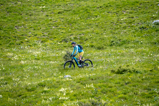 Woman riding electric mountain bike at green meadow grass hills nature landscape wide shot