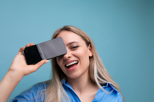 close-up of a happy european blonde girl holding a smartphone screen with a mockup for an application near her face on a blue background.