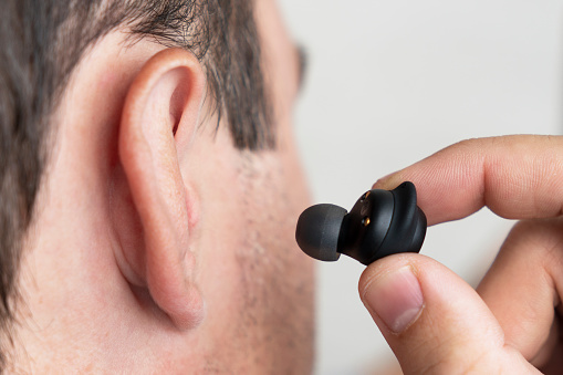 Close-up of wireless earphone in human ear on white background. insert the earphone into the ear