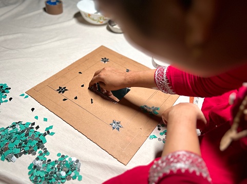 Woman pasting small pieces of mirrors on a wooden board with glue to decorate.