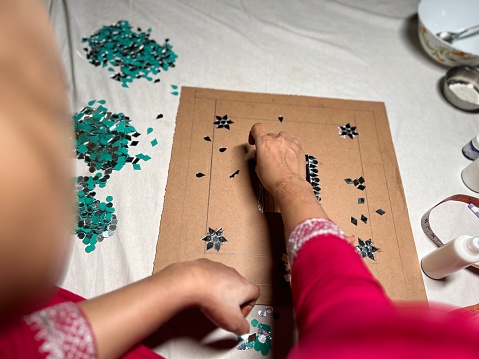 Woman pasting small pieces of mirrors on a wooden board with glue to decorate.