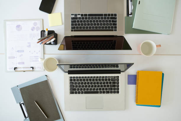 Laptops, documents and planners on office desk, view from above