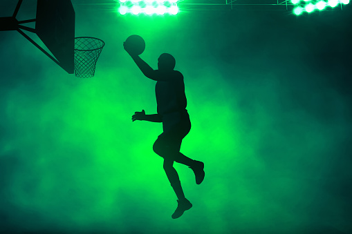 3d illustration shadow silhouette of professional basketball player layup on dark green smoke background
