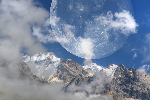 Huge moon over snow-capped mountains. The image of the moon was obtained by the author through a telescope and combined with a photograph of the mountains.