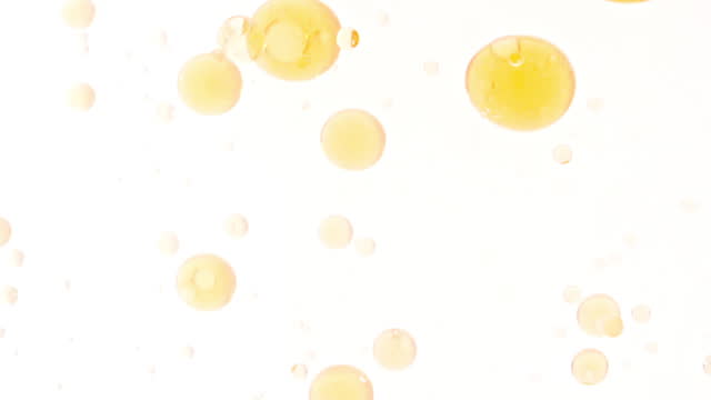 Slow Motion of Moving Yellow Golden Oil, Air Bubbles in Water Rising up on Light White Background. Transparent cosmetic gel fluid with bubbles. Macro Shot.