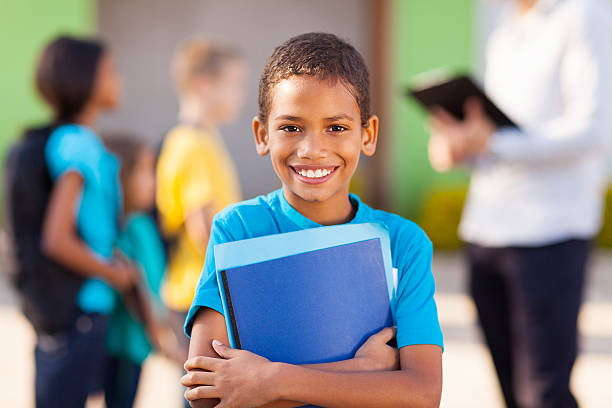 Young male student holding folders and smiling cheerful african male elementary school student holding text books textbook photos stock pictures, royalty-free photos & images