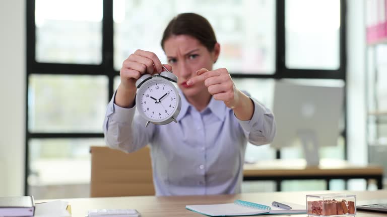 Young strict business woman pointing finger at alarm clock