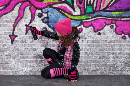 Teenager girl painting a graffiti on a wall.