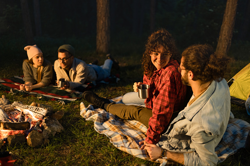Two happy couples relaxing on camping during the evening in nature. Focus is on woman talking to her boyfriend. Copy space.