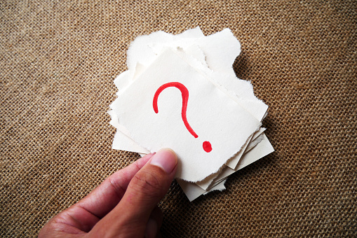 Question mark paper. Torn paper holding hand with question mark on burlap background