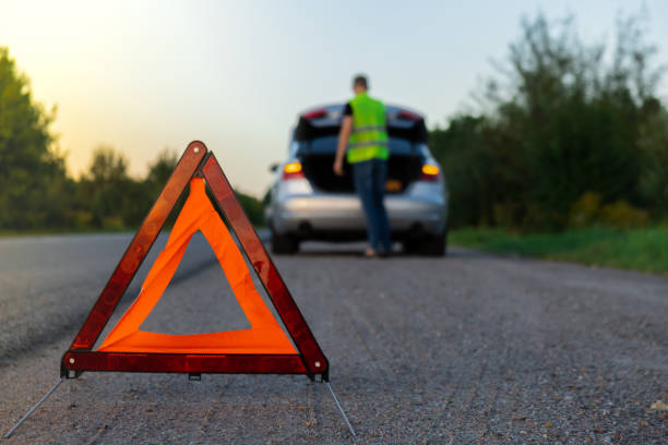 istock Broken silver luxury car emergency accident. Man driver installing red triangle stop sign on road. Sport automobile turned on blinkers technical problems on the road. Safety procedure vehicle broken down 1851682682