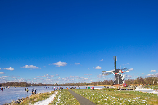 Typical winter landscape in Holland (the Netherlands) with a windmill, a canal, snow, ice and fog.
