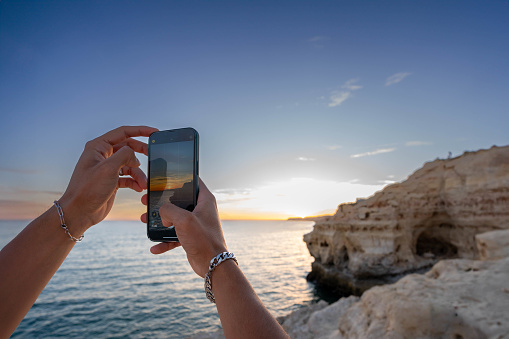 Golden Hour Moment: Young Man Hands Capturing the Ocean Sunset of beautiful cliff shore