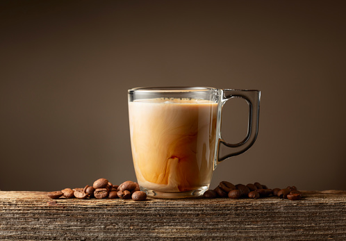 Glass cup of coffee drink, latte or mocha on a brown background. Coffee cup and roasted coffee beans on a old wooden board.