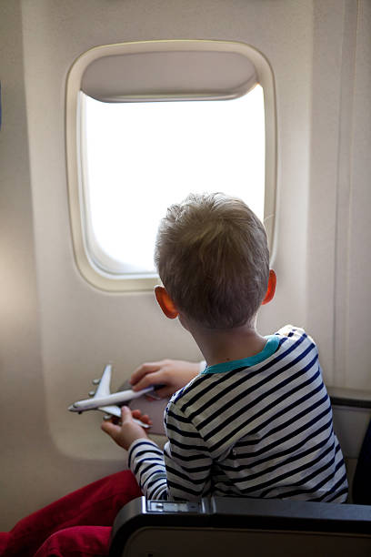 istock Little boy holding toy airplane looking out airplane window 185170698