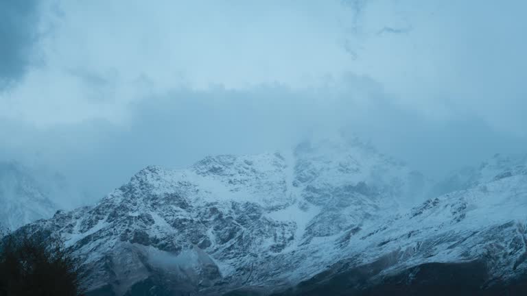 Winter mountain timelapse on the Himalayas. Dark storm clouds moving over snow covered mountain peaks in Keylong, Lahaul, India. Moody winter weather. Winter landscape.