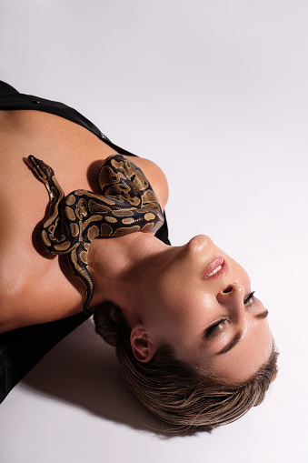 Beautiful woman with python snake elegantly slithering over her body.