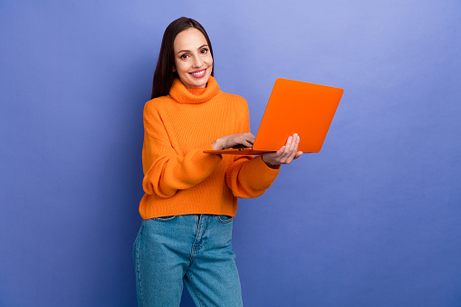 Foto de una mujer de negocios madura en jersey de moda de punto naranja sosteniendo el modelo macbook pro para trabajar aislado sobre fondo de color púrpura photo