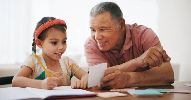 istock Child, senior man and learning or reading, book and education at home, drawing and support or paper. Girl, grandfather and notebook or tutoring, assessment and smile for language or math homework 1851807626