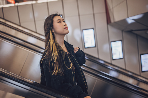 Young Asian woman riding on escalator in subway station in Vienna.