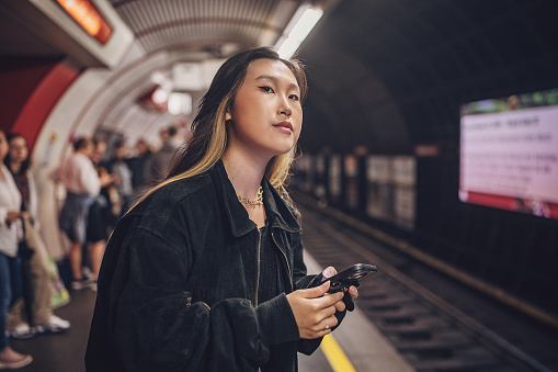 Young Asian woman using smart phone while standing subway platform in Vienna.