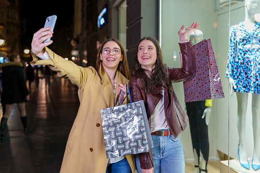 Capture a picture-perfect moment as two female friends strike a pose and capture a stylish selfie in front of a mesmerizing store window