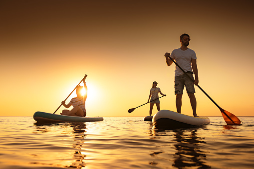 Silhouettes of group of peoples are relaxing on paddle boards at sunset calm lake. Beach weekend concept
