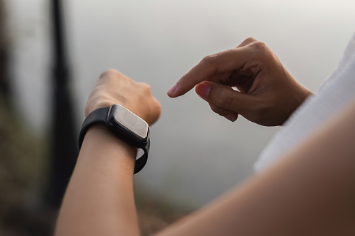 Young Asian woman uses smart watch while jogging at the park..