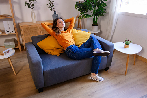 Relaxed young woman sitting on sofa in living room at home.
