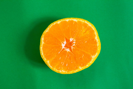 Slice of tangerine or mandarin isolated on a green background. Top view, flat lay.