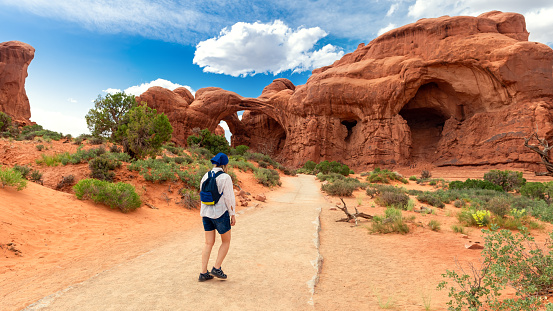 Woman Hiking to the Double Arch Sandstone Rock Formation. The Windows Section Trail with Doble Arch, Natural Wonder in Arches National Park, Utah, United States.
