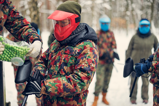 Teenage kids getting ready for winter paintball fun. Teenage boy is receiving paintball balls.\nThey are wearing military uniforms.\nShot with Canon R5